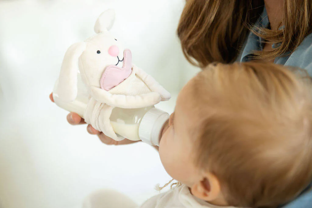 Baby drinking from a bottle with milk in it that has a bottle-lovey on it.
